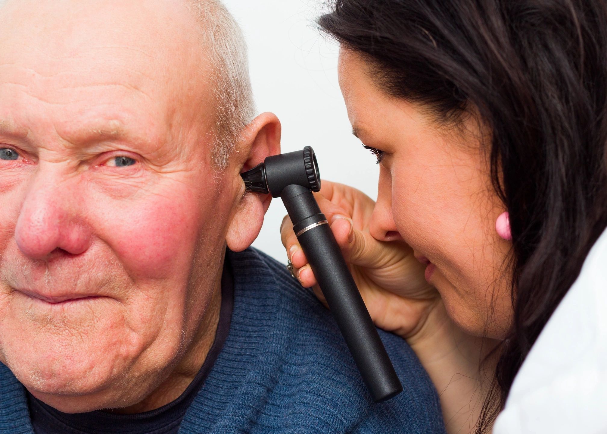 A woman is putting an ear piece on the ear of an older man.